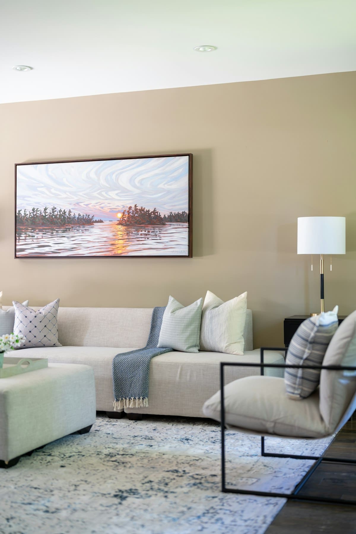 Pintura de paisagem lacustre ao pôr do sol sobre um sofá claro numa sala de estar quente