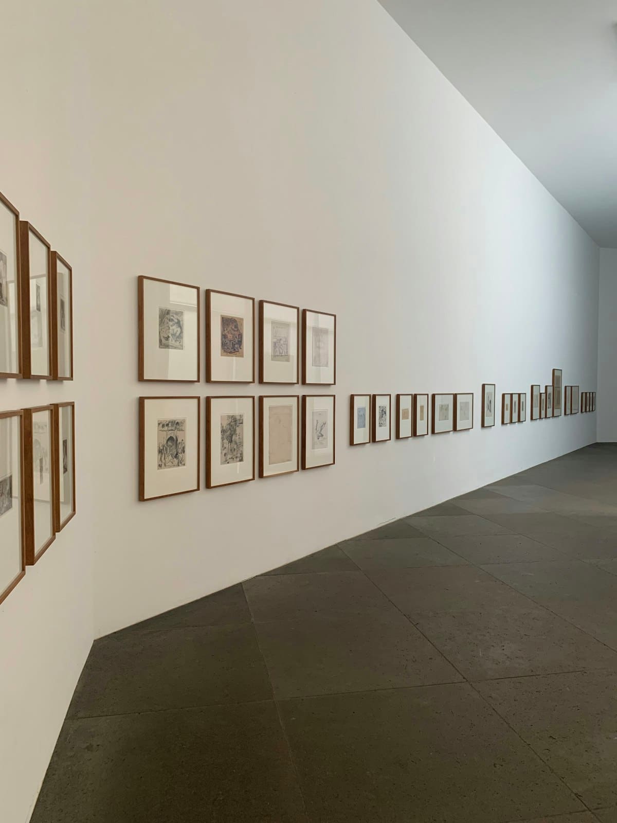 Fileira de pequenas estampas emolduradas ao longo de um corredor de galeria luminoso